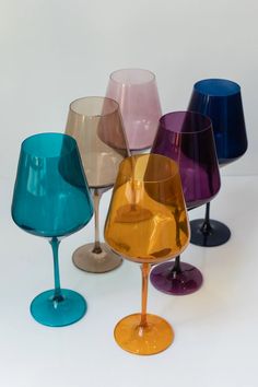 several different colored wine glasses sitting next to each other on a white surface with one empty glass in the middle