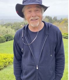 an older man wearing a hat standing in the grass