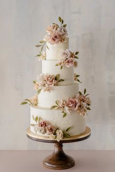 a white wedding cake with pink flowers on top and greenery around the edges, sitting on a wooden stand