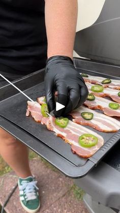 a person in black gloves is cooking bacon and jalapenos on a grill