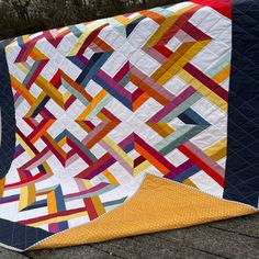 a colorful quilt sitting on top of a wooden table next to a tree trunk and fence