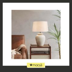 a white lamp sitting on top of a table next to a brown chair and potted plant