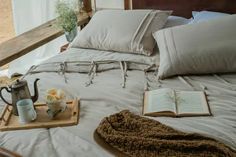 an open book on a bed next to pillows and a tray with coffee mugs