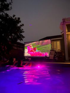 people are sitting in the pool watching a movie at night with purple lights on it