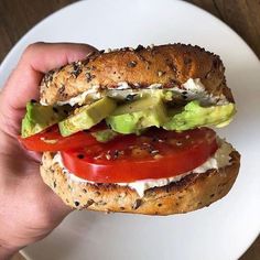 a sandwich with tomatoes, lettuce and cheese on a bagel bun is held up by someone's hand