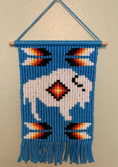 a blue beaded wall hanging with white and orange designs