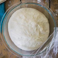 a glass bowl filled with dough on top of a wooden table