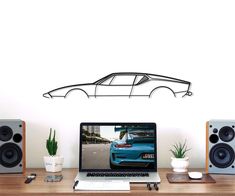 a laptop computer sitting on top of a desk next to speakers and a car wall decal