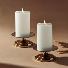 two white candles sitting on top of each other in front of a brown background with feathers