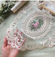 a hand is touching the edge of a piece of white lace with pink flowers on it