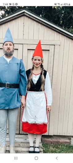 two people dressed up as gnomes standing in front of a shed, one wearing an orange hat