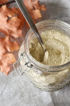 a glass jar filled with white powder next to leaves on a gray cloth and a spoon in it