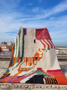 a large multicolored rug is on the ground in front of a fence and blue sky