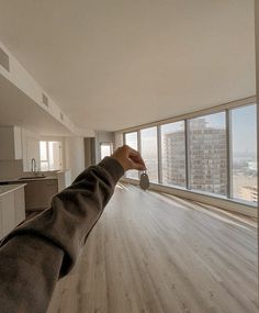 a person's hand reaching out towards an empty room with large windows and wood flooring