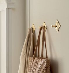 two purses hanging on the wall next to towels and coat hooks in a white room