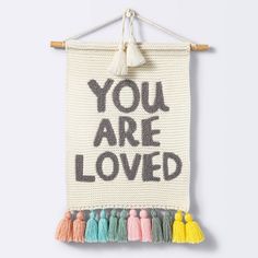 a wall hanging with the words you are loved written on it and tassels