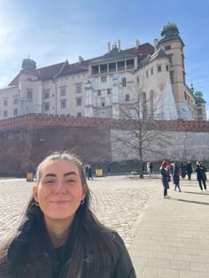 a woman standing in front of a large building with people walking around it on a sunny day