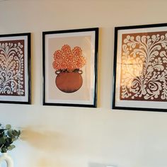 three framed art pieces hang on the wall above a table with a vase and potted plant