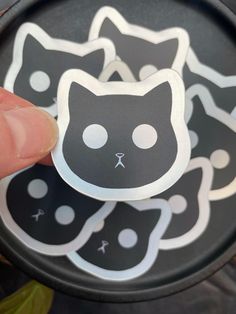 a person holding a sticker in front of a frying pan with black and white cats on it