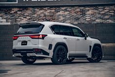 the rear end of a white suv parked in front of a brick building with black rims