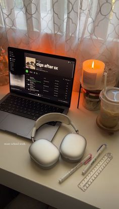 an open laptop computer sitting on top of a desk next to headphones and candles