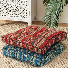 three colorful cushions stacked on top of each other in front of a white cabinet and potted plant