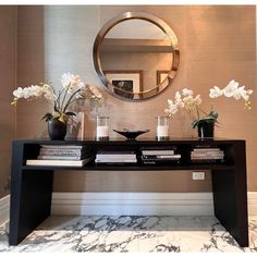 a console table with books and vases on it in front of a wall mirror