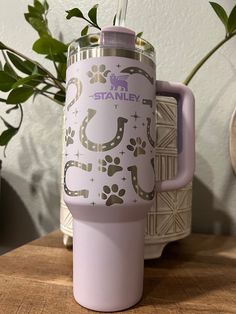 a pink travel mug sitting on top of a wooden table next to a potted plant