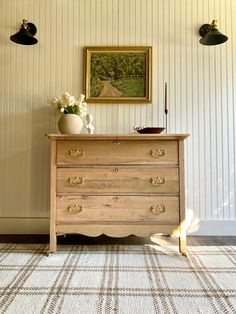 a wooden dresser sitting in front of a wall with two lamps on top of it