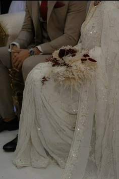 two people sitting next to each other on a white floor wearing wedding dresses and holding bouquets