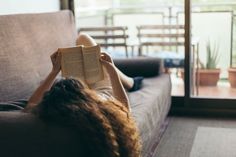 a woman laying on top of a couch holding an open book in her hands while reading