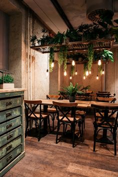 an empty restaurant with wooden tables and green plant hanging from the ceiling, along with two dressers