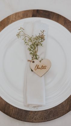 a white plate topped with a wooden heart shaped decoration and greenery on top of it