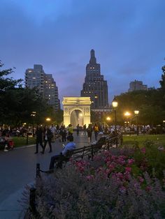 people are sitting on benches in the park at night with tall buildings in the background