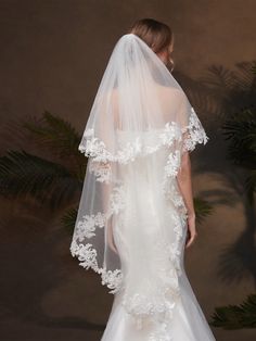 a woman in a white wedding dress with a veil over her head and flowers on it