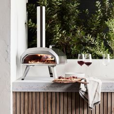 a pizza oven sitting on top of a counter next to two glasses of red wine