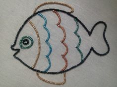 a fish made out of beads on a white tablecloth with gold and blue trimmings