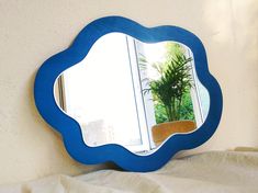 a blue mirror sitting on top of a white bed next to a potted plant