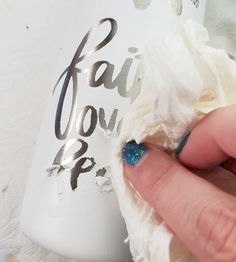 a person with blue nail polish on their nails is peeling the fabric off of a white bottle