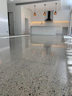 an empty kitchen with white cabinets and marble flooring is pictured in this image, there are three pendant lights hanging from the ceiling