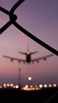 an airplane is taking off from the runway at night, as seen through a chain link fence