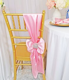 a chair with a pink sash on it next to a plate and flower vases