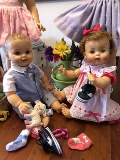 two dolls sitting next to each other on a wooden floor with flowers in the background