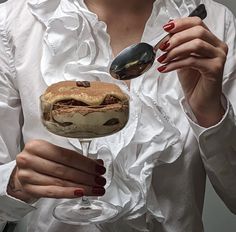 a woman with red nails holding a sandwich and spoon in her hand while wearing a white shirt