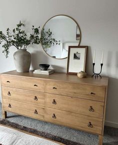 a wooden dresser with two vases and a mirror on top of it next to a bed