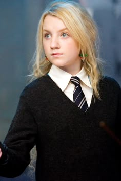 a woman with blonde hair wearing a black sweater and striped tie, looking off to the side