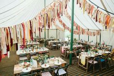 tables and chairs are set up in a large tent with colorful ribbons hanging from the ceiling