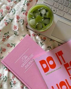 two pink books sitting on top of a bed next to a cup of green tea