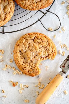 two cookies on a cooling rack with a knife next to it and some oatmeal in the background