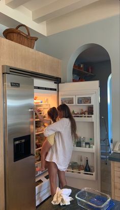 two people are standing in front of an open refrigerator and looking into the freezer